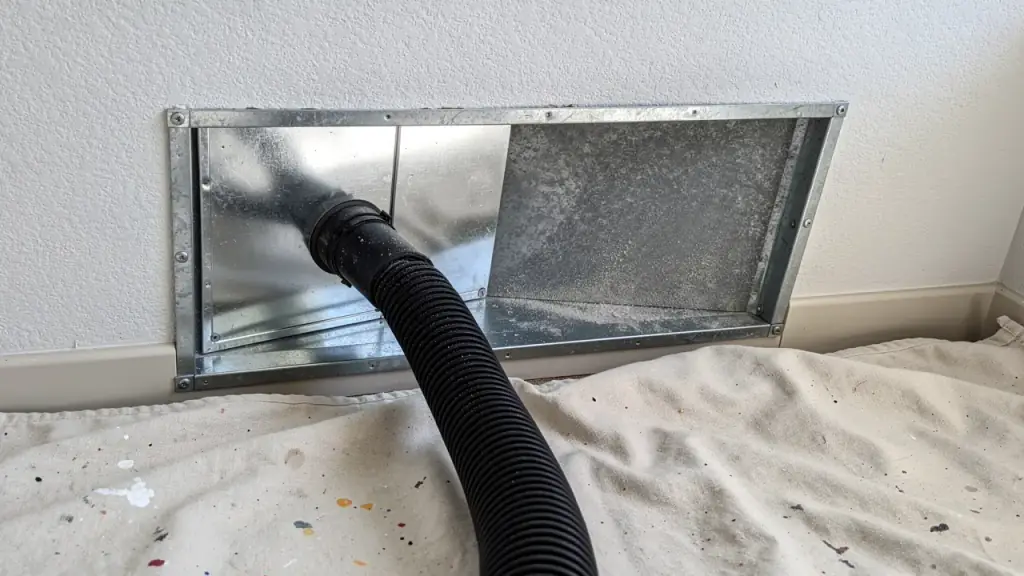 A supply register removed over a drop cloth with a vacuum hose fed into the galvanized duct